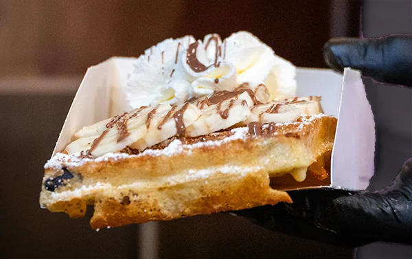 Een warme wafel met verse bananenschijfjes, slagroom en chocoladesaus